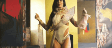 a woman in a white bodysuit and gloves is dancing in front of a wall with graffiti on it .