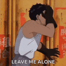 a man in a white tank top and black gloves is covering his face with his hands and says leave me alone .