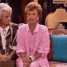 two women are sitting on a couch and one is wearing a pink outfit