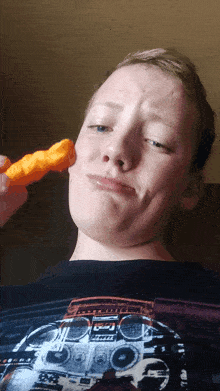 a young man wearing a black shirt with a boombox on it is eating a cheetos