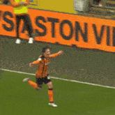 a soccer player in an orange and black uniform is running on a soccer field