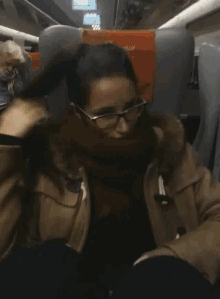 a woman wearing glasses is sitting on a train with a trenitalia seat cushion