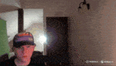 a man wearing a hat with a picture of a sunset on it stands in a room with a light on the wall