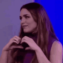 a woman in a purple top is making a heart with her hands .