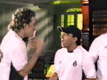 a man wearing a white shirt with a soccer ball on it talks to another man