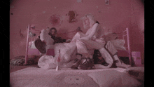 a man and a woman sit on a bed in a pink bedroom