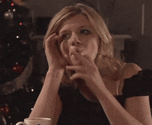 a woman sitting at a table with a cup of coffee and a christmas tree in the background