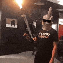 a man wearing a black shirt that says occupy mars is holding a gun and giving the middle finger .