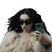 a woman wearing sunglasses and a fur coat takes a selfie with her phone