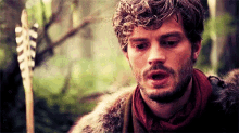 a man with curly hair and a beard is holding an arrow in his hand .