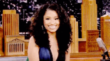a woman with curly hair and a plunging neckline is smiling in front of a city skyline .