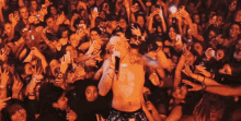 a shirtless man sings into a microphone in front of a crowd