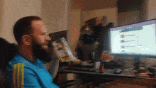 a man in a blue shirt with yellow stripes sits in front of two monitors