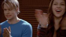 a man and a woman are clapping their hands in front of a wooden wall