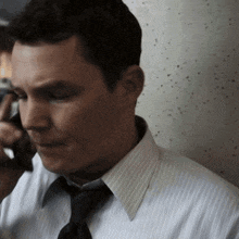 a man in a striped shirt and tie is talking on his cell phone