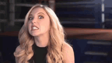 a blonde woman is making a funny face with her mouth open while wearing a black top .