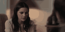 a woman is sitting at a table talking to another woman while looking at the camera .