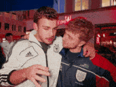 a man wearing a white adidas jacket hugs another man
