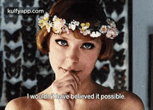 a woman with a flower crown on her head is holding her hand to her mouth .