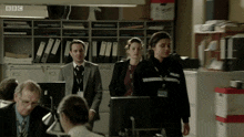 a group of people in an office with a bbc logo on the ceiling