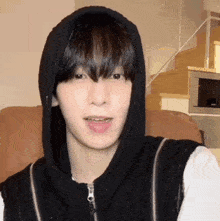 a young man wearing a black hoodie is sitting on a couch in a living room .