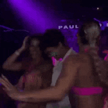 a man in a white shirt is standing next to two women in pink bikinis .
