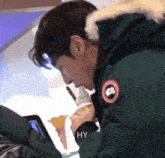 a man wearing a green parka with a fur hood is eating an ice cream cone