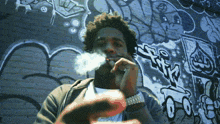 a man smoking a cigarette in front of a wall with graffiti on it that says ' a '
