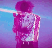 a man in a white shirt is holding a microphone in front of a purple light .