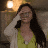 a woman wearing a green top and a white cardigan drinks from a glass
