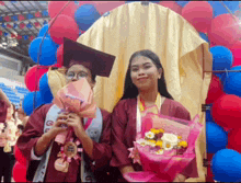 two female graduates are holding bouquets of flowers