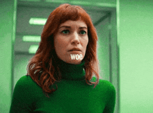 a woman with red hair is wearing a green turtleneck sweater with the word woe written on her face .