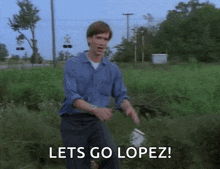 a man in a blue shirt is standing in a field holding a bucket and saying lets go lopez !