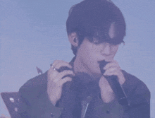 a man with glasses and a ring on his finger sings into a microphone