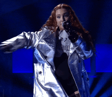 a woman singing into a microphone in a silver coat