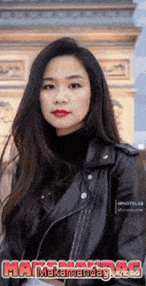 a woman wearing a black leather jacket is standing in front of a building .