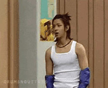 a man wearing a white tank top and blue gloves is standing in a room .