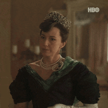 a woman wearing a pearl necklace and a tiara with hbo on the bottom right