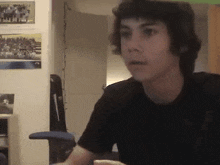 a young man in a black shirt is sitting in a chair