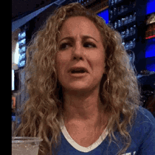 a woman with curly hair is wearing a blue shirt that says ' t.j. ' on it
