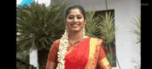 a woman wearing a red and gold saree is smiling