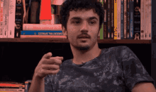 a man in a black shirt is pointing at something in front of a bookshelf full of books including one called essential space