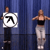 a man and a woman are dancing in front of a blue curtain with an a logo in the background