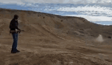 a man is standing in the desert holding a gun and shooting it .