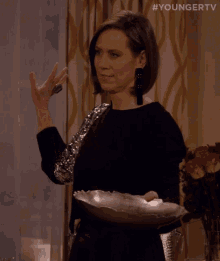 a woman in a black dress is holding a silver plate and making a funny face .