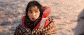 a woman is wrapped in a blanket and wearing a life jacket while looking at the water .