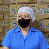 a woman wearing a mask in front of a stack of block buster boxes