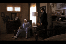 a man in a suit sits in a chair in a living room next to a boy