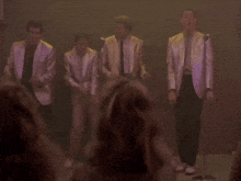 a group of men in suits are singing into microphones in front of a crowd