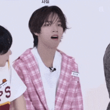 a young man wearing a pink plaid jacket and a white t-shirt with ps on it